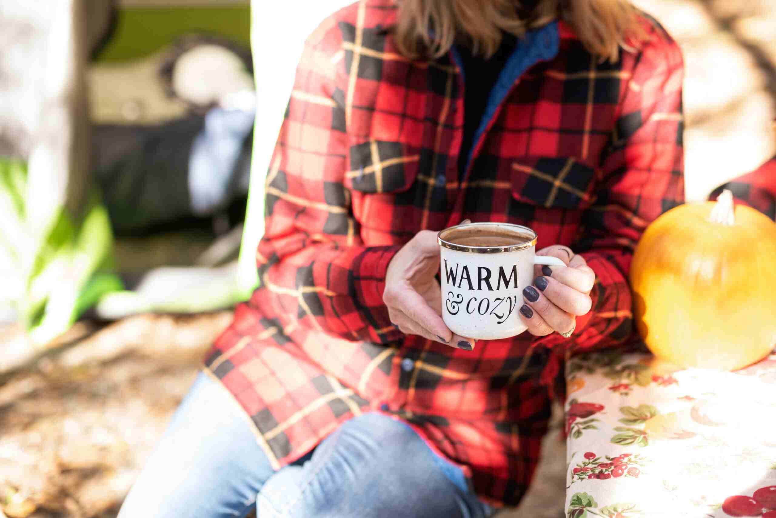 woman in red plaid holds coffee cup that says warm and cozy