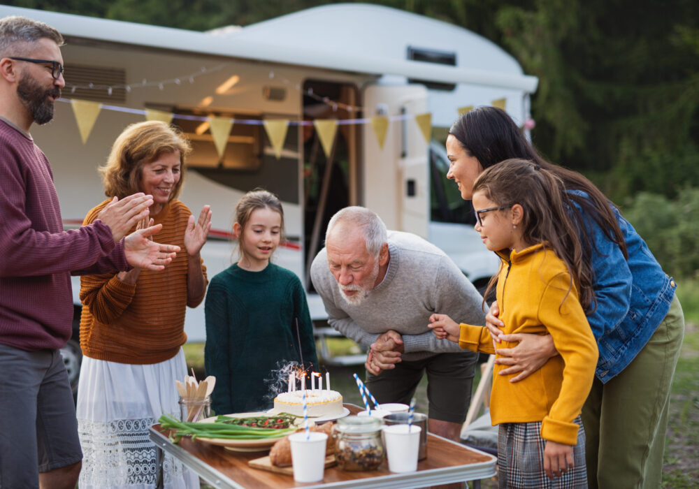 A multi-generation family celebrating birthday outdoors at campsite, caravan holiday trip.