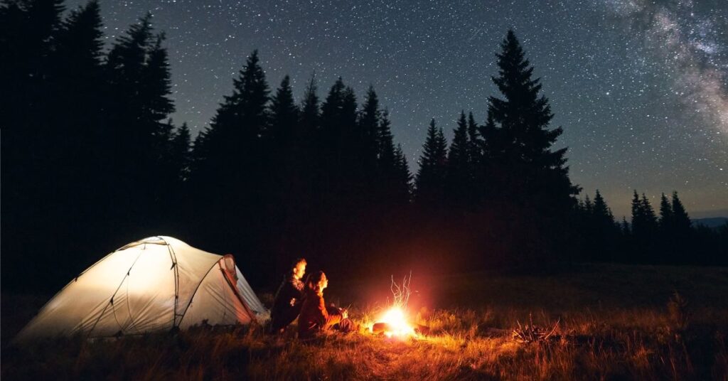 couple by campfire and tent at night
