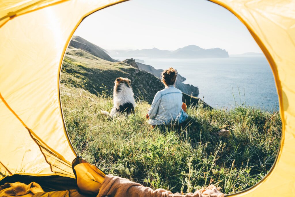 woman-traveling-with-dog-in-front-of-tent-scenic-seashore-view