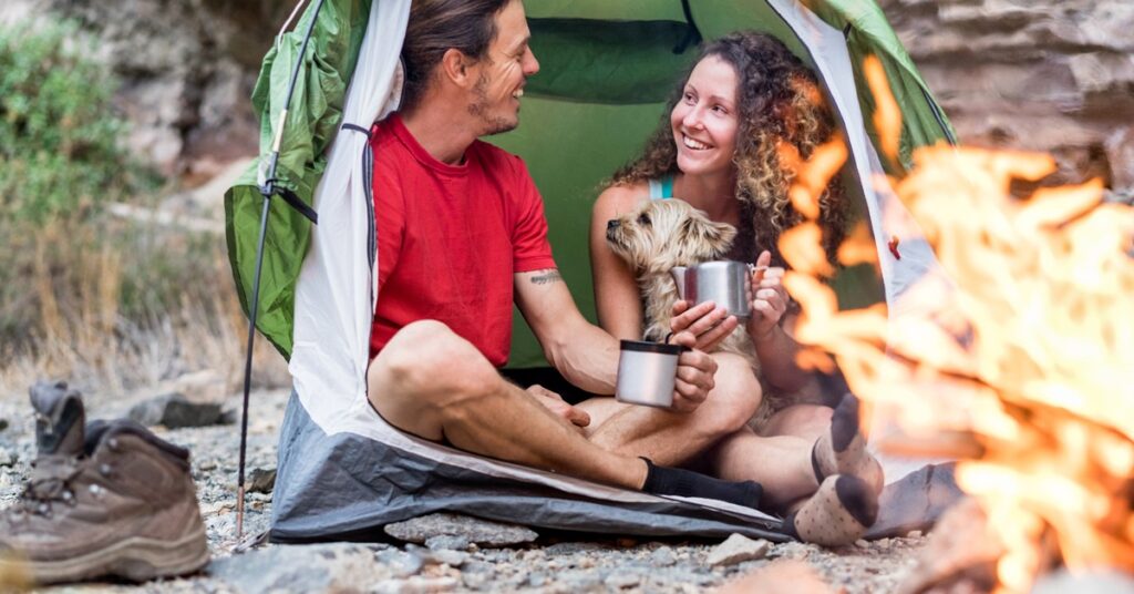 couple-camping-in-tent-with-dog-drinking-coffee