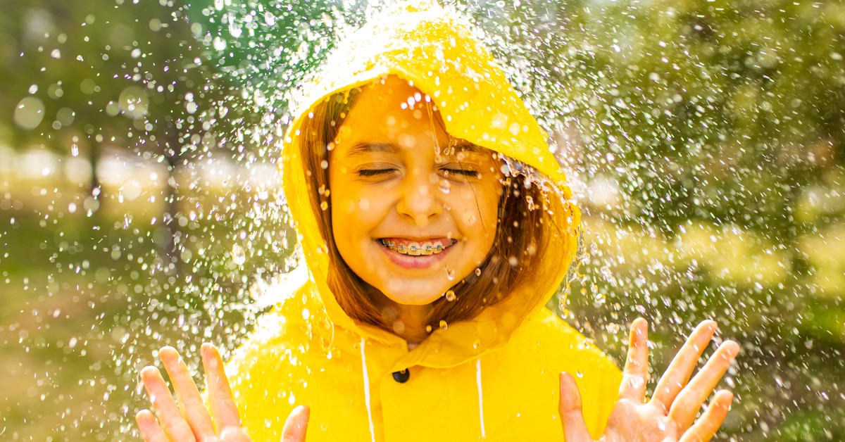 young-girl-smiling-in-the-rain-wearing-bright-yellow-rain-jacket