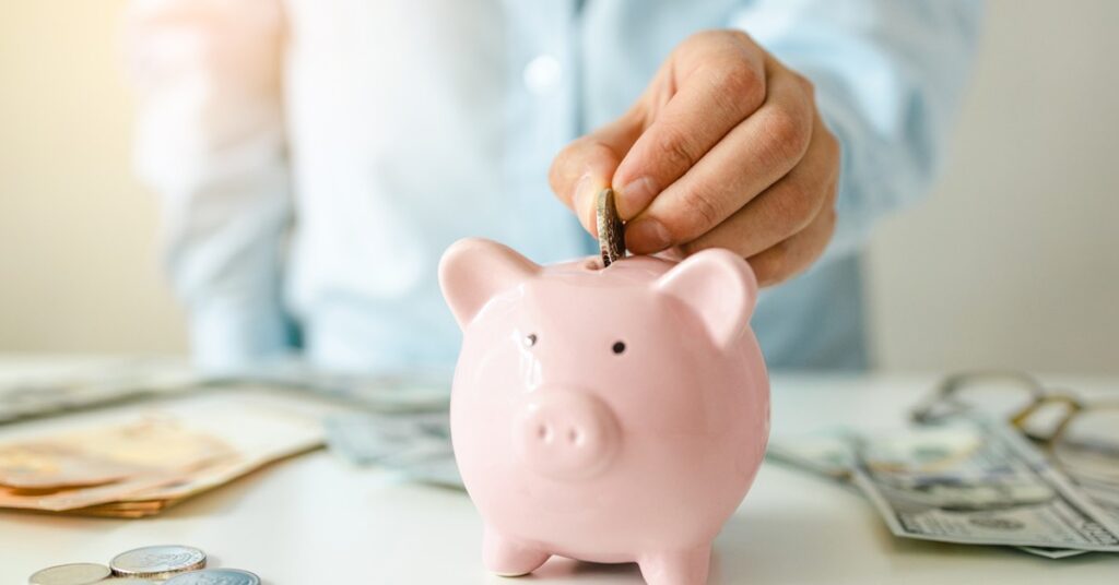 man's hand placing coin into pink piggy banks