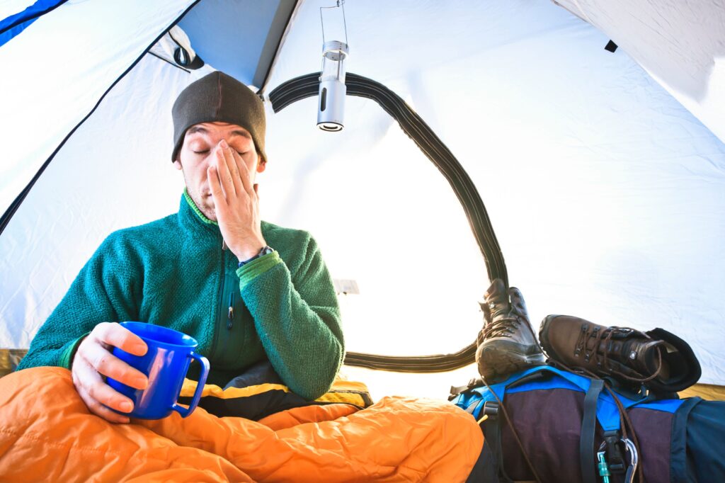 man-waking-up-in-a-tent-holding-mug-of-coffee-and-rubbing-his-eyes