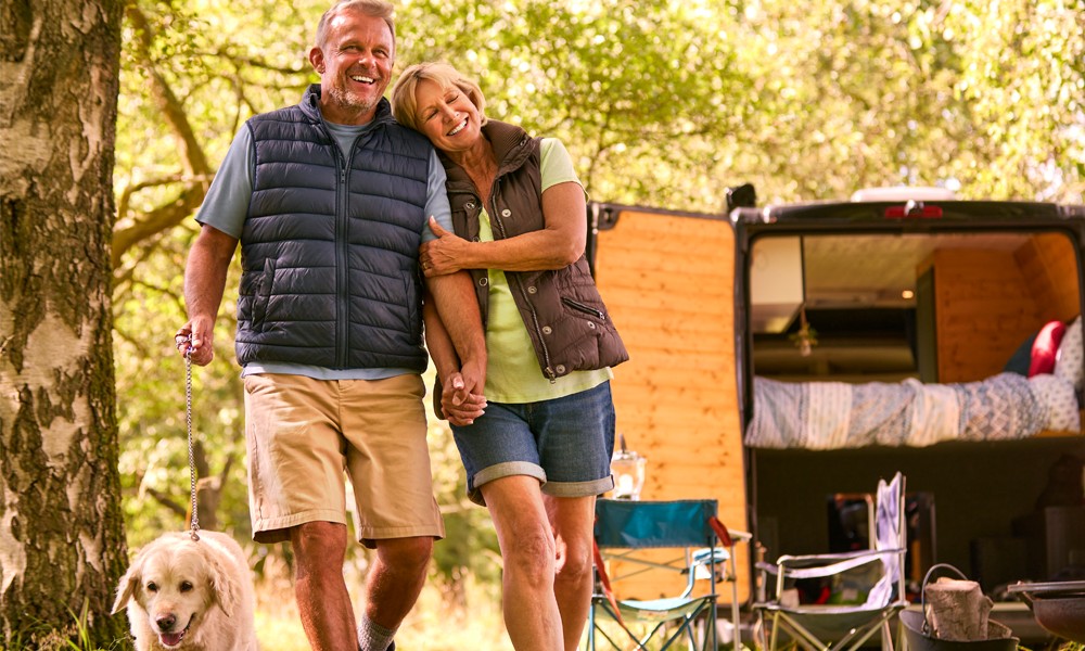 older couple with dog smiling in front of their camper van