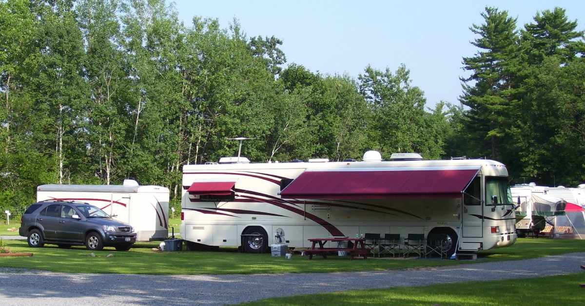 large camper rv by other campers and a car, there are tables and chairs set out
