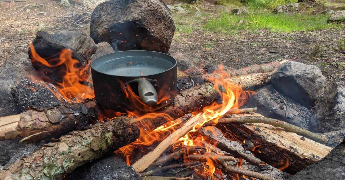 water in a pot set over a campfire ready to boil