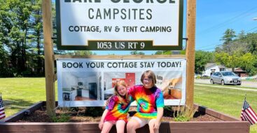 sisters in tie dye t-shirts posing in front of the Lake George Campsites main sign
