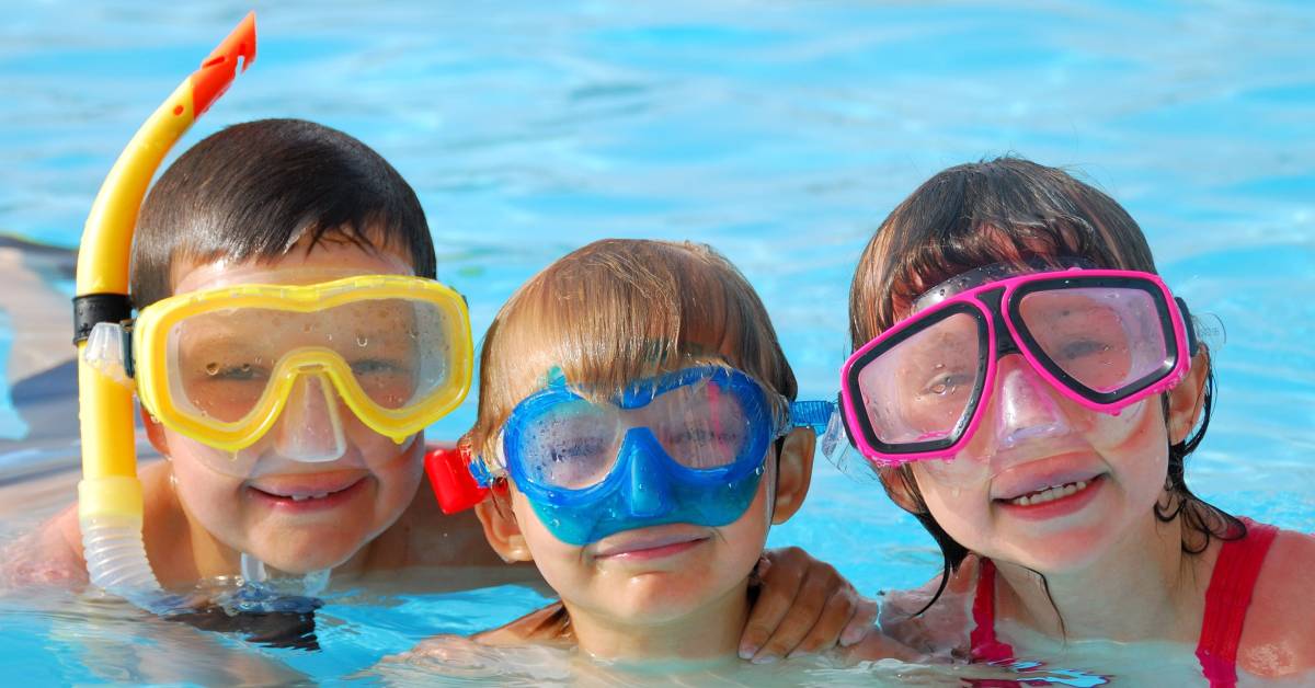 three kids in pool pose with goggles on