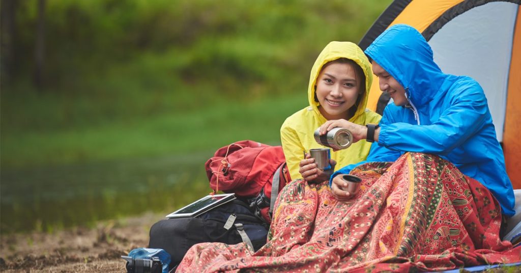 couple tent camping in the rain wearing rain coats, drinking tea