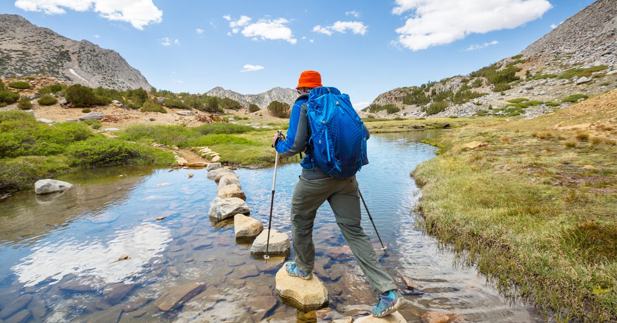 man hikes with hiking poles on stepping stones over stream