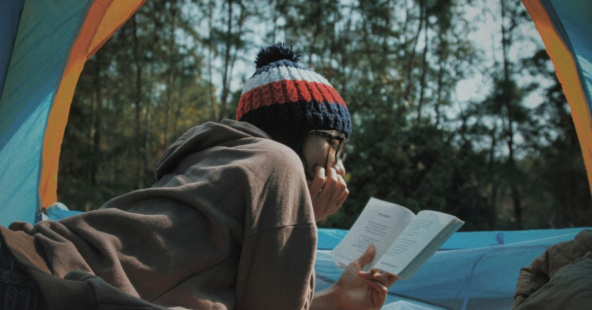 woman reading a book in a tent with a forest in the background