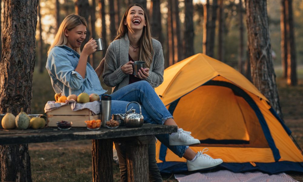 Female friends enjoying a hot beverage while camping in the woods in the fall season